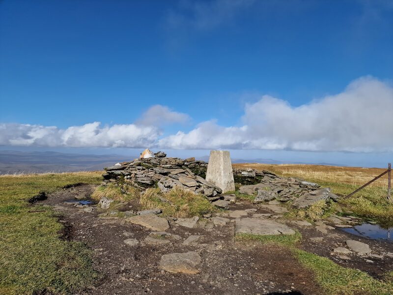 The trig pillar and its low stone shelter on the summit of Ben Wyvis under a blue sky.