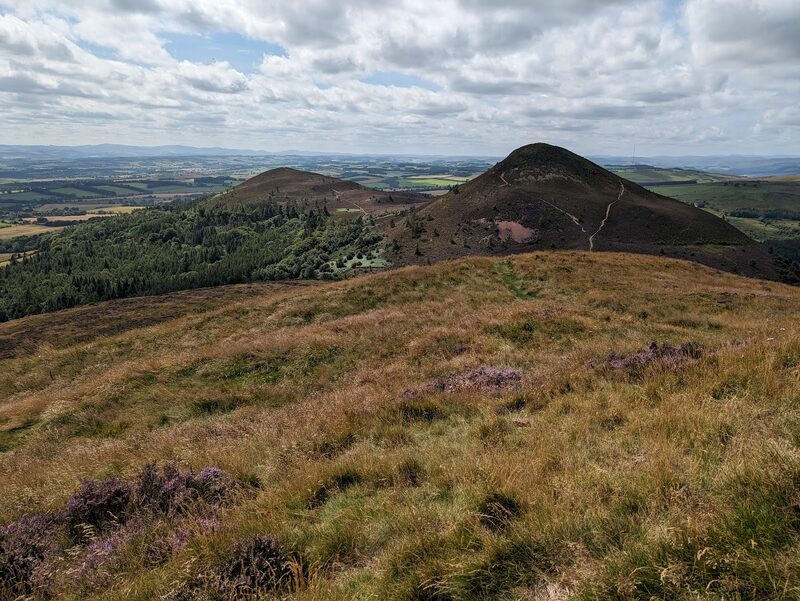 Path winding over heather-covered hills towards farmland and distant peaks
