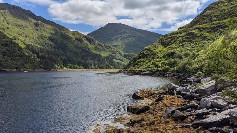 Sgurr a' Mhaoraich standing over the head of a sea loch, with steep green slopes on either side and a rocky shore in front.