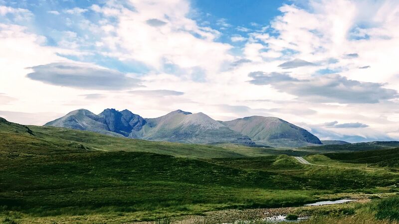 The whole of An Teallach on the skyline, its jagged tops and rounder shoulders above green moor under a broken sky.