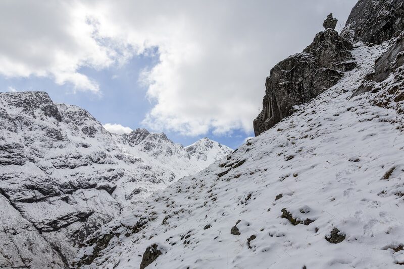 A snow slope under dark crags, with a line of snowy tops beyond.
