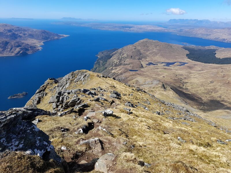 The view from high on Beinn Sgritheall down its rocky ridge to lochans and the blue water of Loch Hourn.