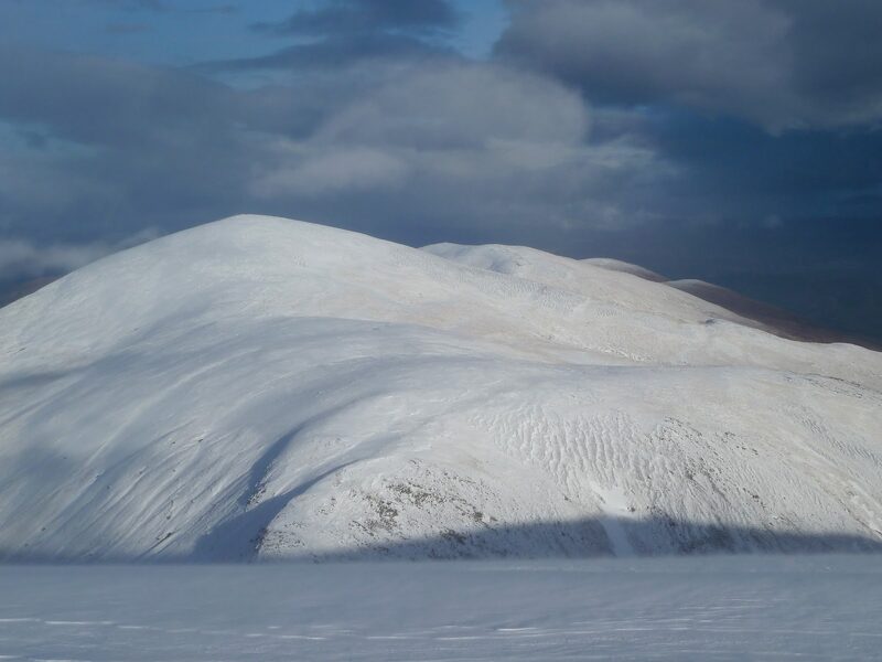 The rounded dome of Toll Creagach under full snow, sunlit against a dark sky.