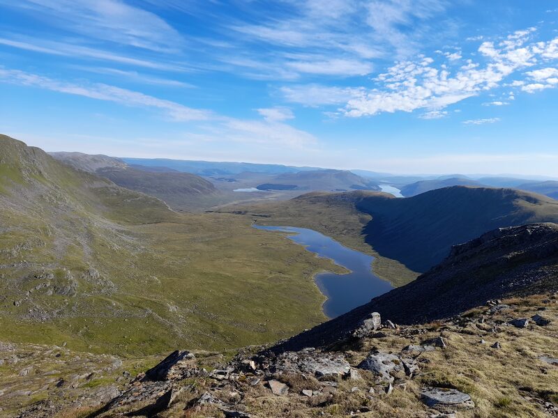 The narrow loch in the trough between Ben Alder's slopes on the left and Beinn Bheoil's long ridge on the right, with more water far off under a blue sky.
