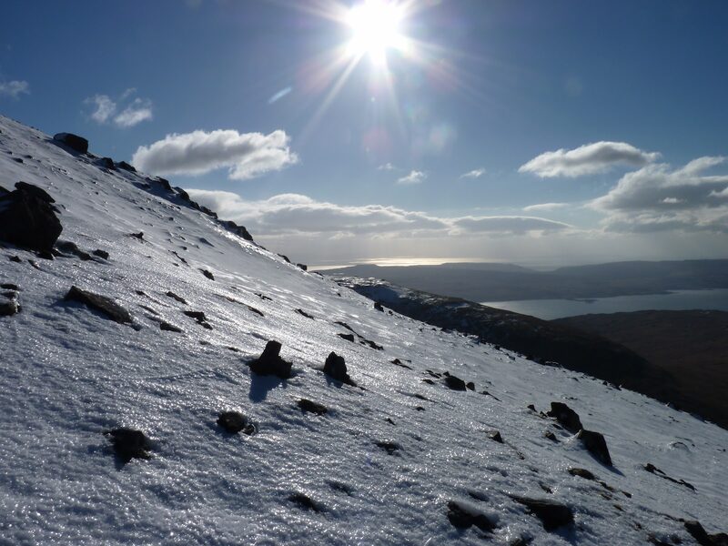 A snow slope on Ben More in low winter sun, the sea and the shore below.