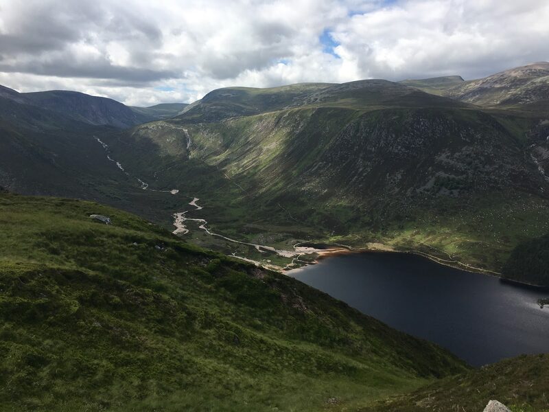 The head of the loch from the hillside above, a pale beach and a burn winding into dark water under steep slopes.
