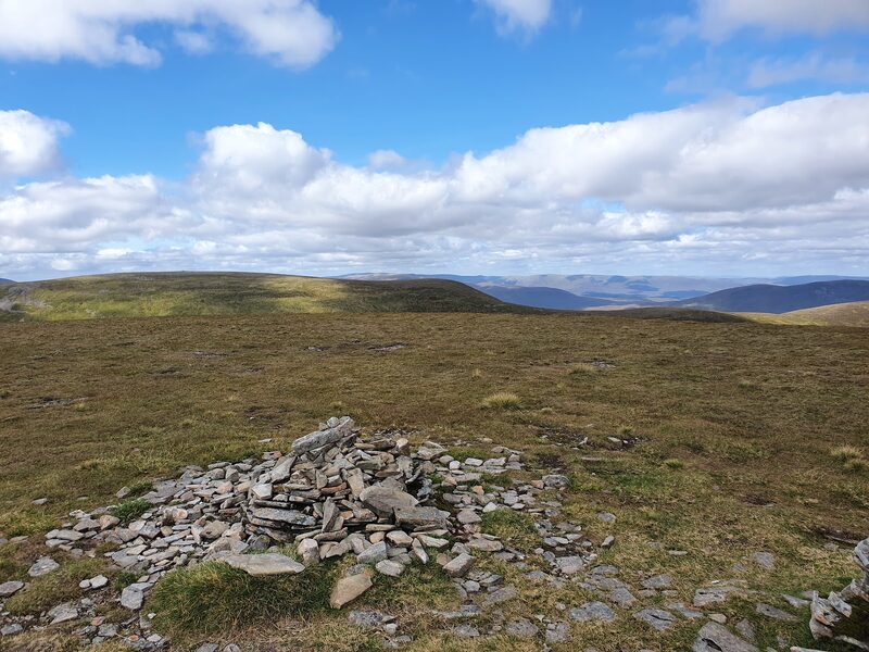 A small cairn of flat stones on the broad mossy top, white cloud over far ridges.