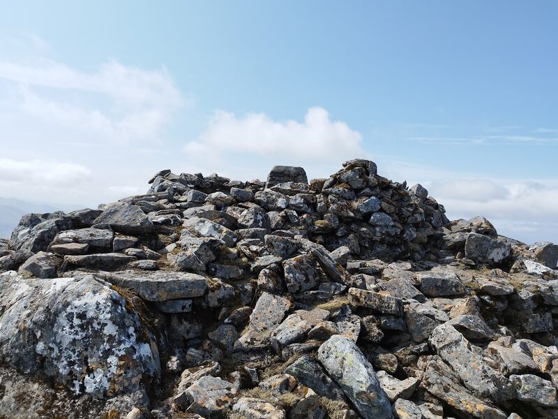 A ring of piled stones on the rocky top of Sgurr na Lapaich, with the cap of a stone pillar showing inside it.