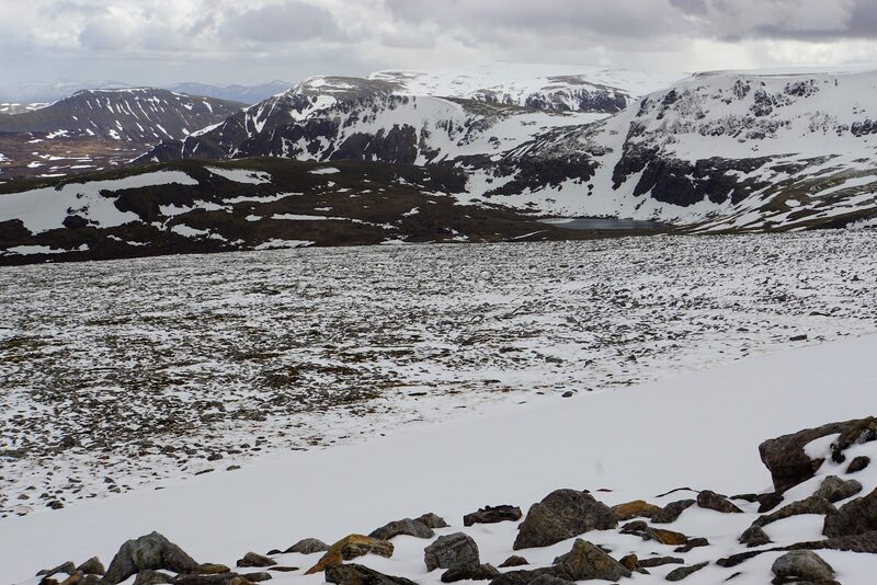 The view from the snowy plateau to corries and a small lochan across the glen.