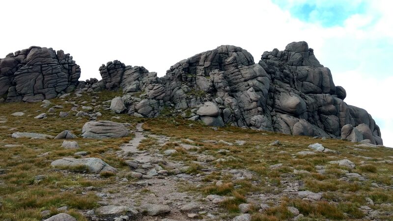 The granite tors of Ben Avon's plateau, with a worn path running up to them over grass and gravel.