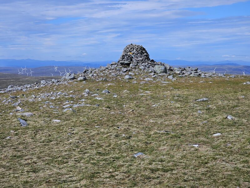 The tall stone cairn on the summit of Geal Charn, with wind turbines on the moor far behind it.