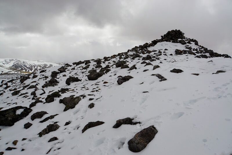 The summit cairn under snow and heavy cloud.