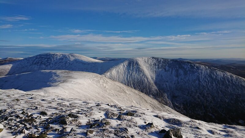 The onward ridge of Beinn a' Ghlò under snow and a blue sky, seen across a deep corrie from the summit.