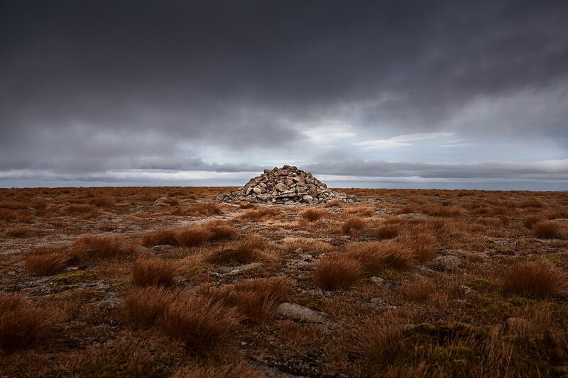 A cairn of stones on the wide, flat summit plateau under dark cloud.