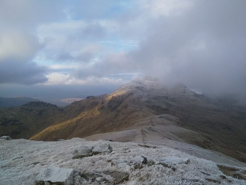 Frosted rock in the foreground and a path running on along the ridge to a summit half in cloud.