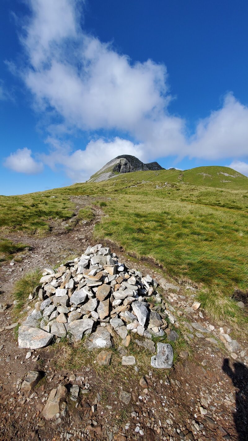The hill's pale, craggy top above a green slope, with a cairn of pale stones on the path in front.