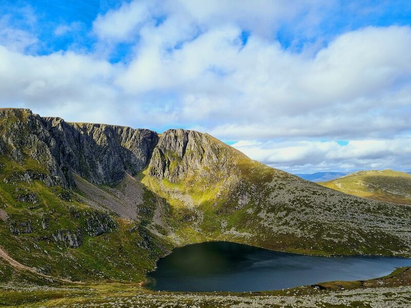 The cliffs of the corrie above its dark loch in sun.