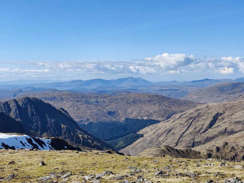 The view from high ground over a deep glen and brown hills to a far line of peaks.