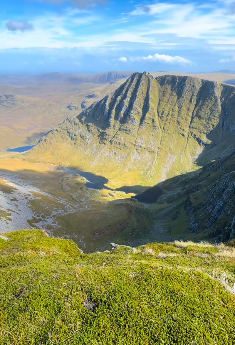 The great cliffs of Seana Bhràigh above a green corrie, seen from the grassy rim.