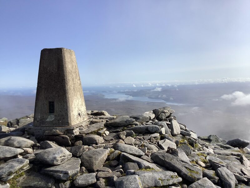 The trig pillar on the bouldery summit of Ben Hope, lochs and cloud far below.