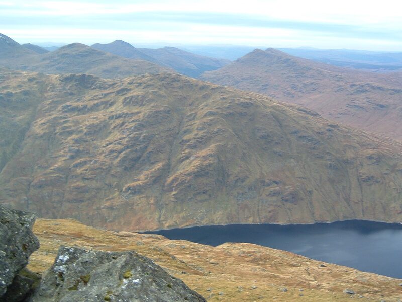 From high on Ben Vorlich, a narrow dark loch far below under a steep brown hillside, with ridge after ridge beyond.