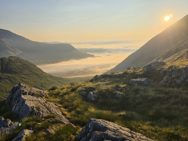 Sunrise from rocks high on the hill, mist filling the glen between dark slopes.
