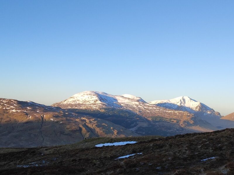 Snow-topped hills catching the last light across a dark moor with patches of old snow.