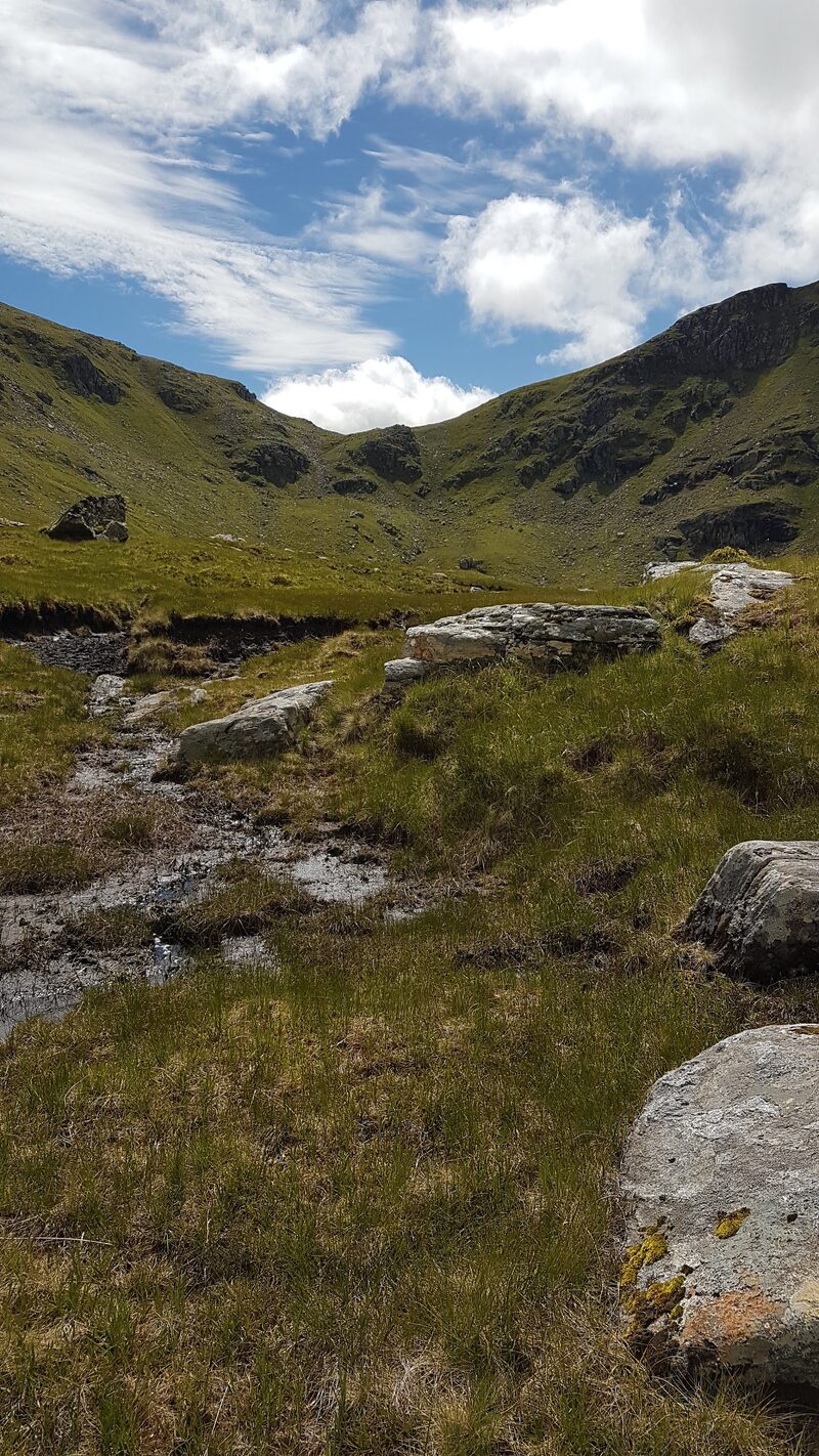 The corrie of A' Chailleach and its skyline, over peat hags and scattered rocks.