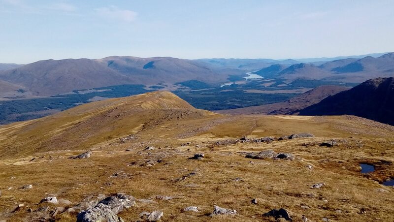 The view from the top down the hill's broad grassy ridge to a wooded strath and a long loch