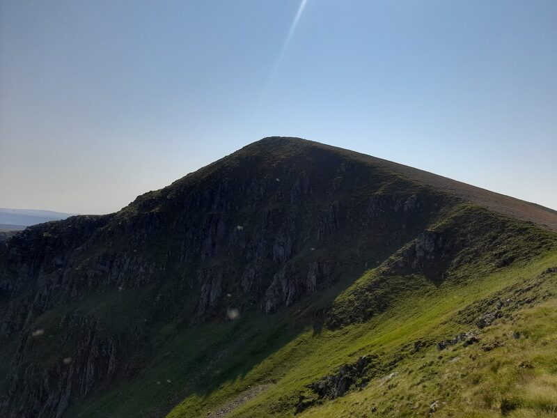 The dark pyramid of Sgùrr nan Conbhairean, grass on its sunlit ridge, under a clear sky.