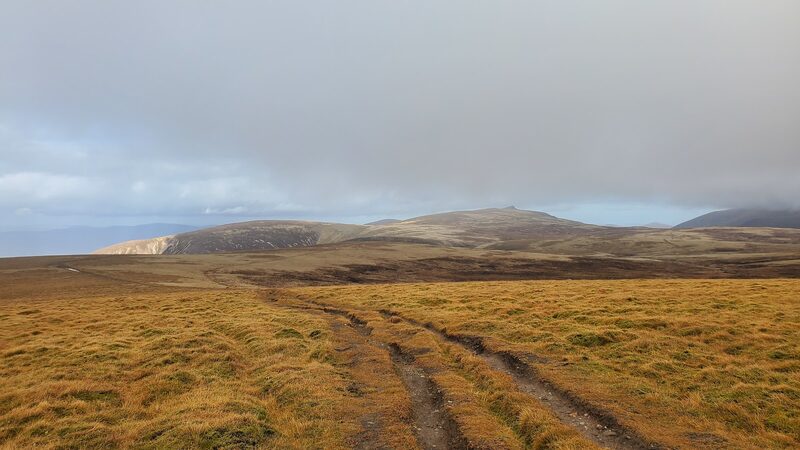 Vehicle tracks crossing the tawny plateau of Mullach Clach a' Bhlàir under heavy cloud.