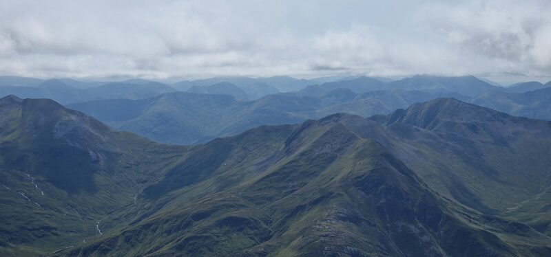The view from high on the hill over green ridges and glens to far ranges under a lid of cloud.