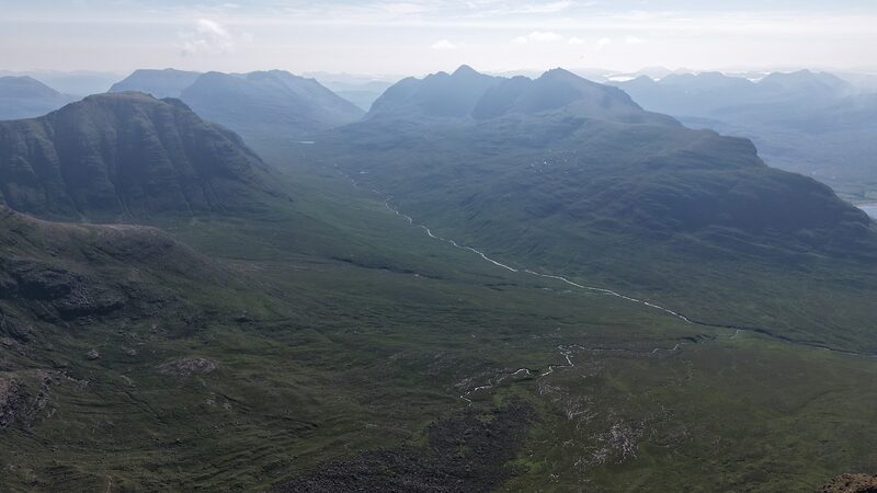 A burn winding down a long green glen between steep-sided hills, from high on Beinn Alligin, in haze.