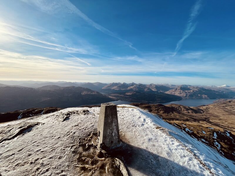 The summit pillar in frost with the loch and the hills beyond.