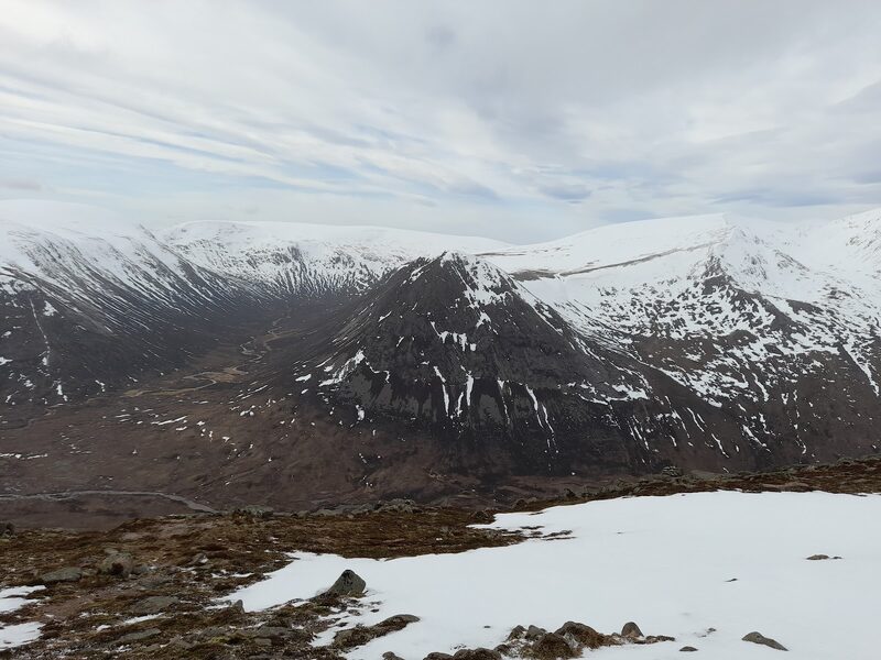 The hill in winter from across the glen: a dark rock face streaked with snow, with white hills behind it.