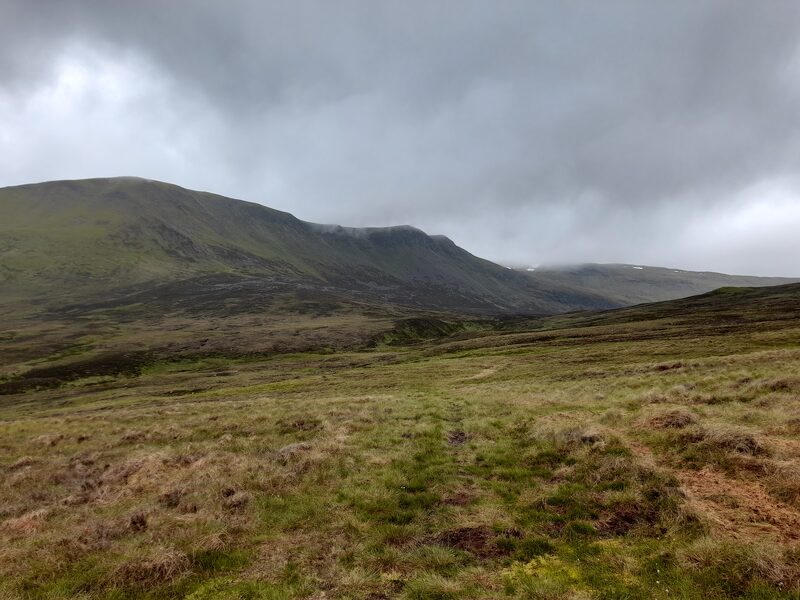 Carn Dearg seen across rough moorland, a rounded top with a rim of crags below its skyline under heavy cloud.