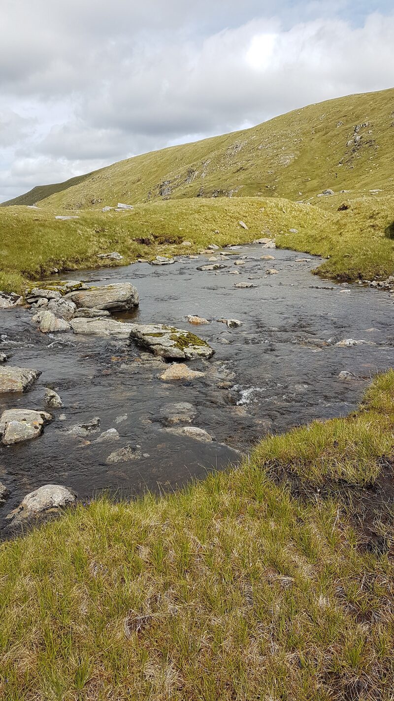 A stony burn running below the grassy slopes of A' Chailleach.