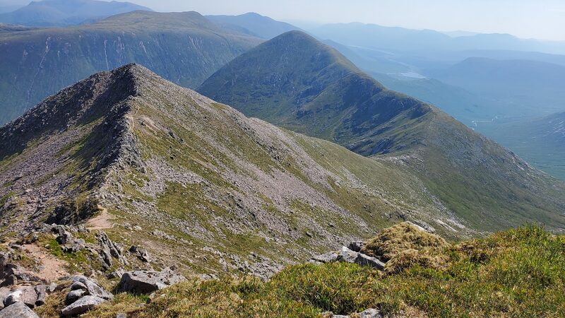 A rocky ridge rising to a pointed top on Glas Bheinn Mhòr, hills in haze behind.