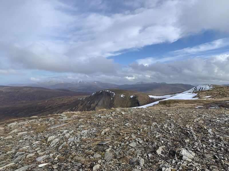The stony summit plateau of Meall Buidhe, with crags dropping from its edge and old snow along the rim.