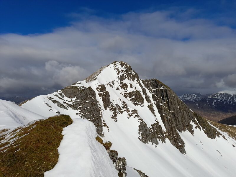 The sharp top of Ciste Dhubh under snow, a dark crag falling from one side, seen along its ridge.