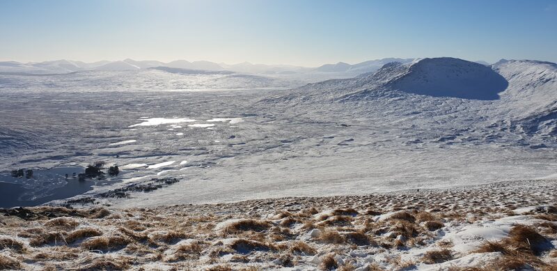 Under snow, the view from the slopes of Beinn na Lap over the wooded islets at the end of Loch Ossian to a hill with a scooped corrie
