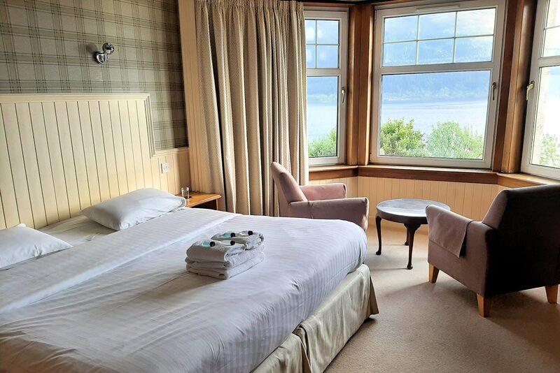 A bedroom with tartan wallpaper and a bay window looking out over Loch Linnhe.