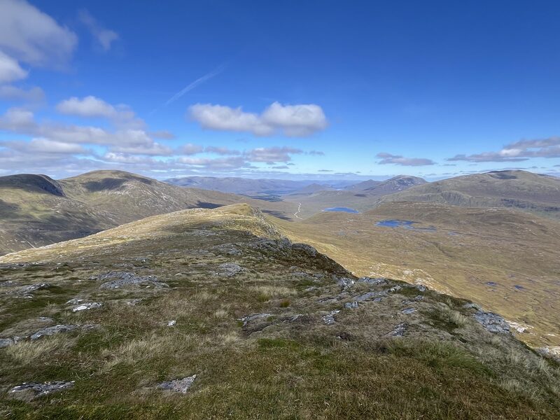 The view along the grassy ridge of Beinn na Lap to small lochans and far hills on a blue day