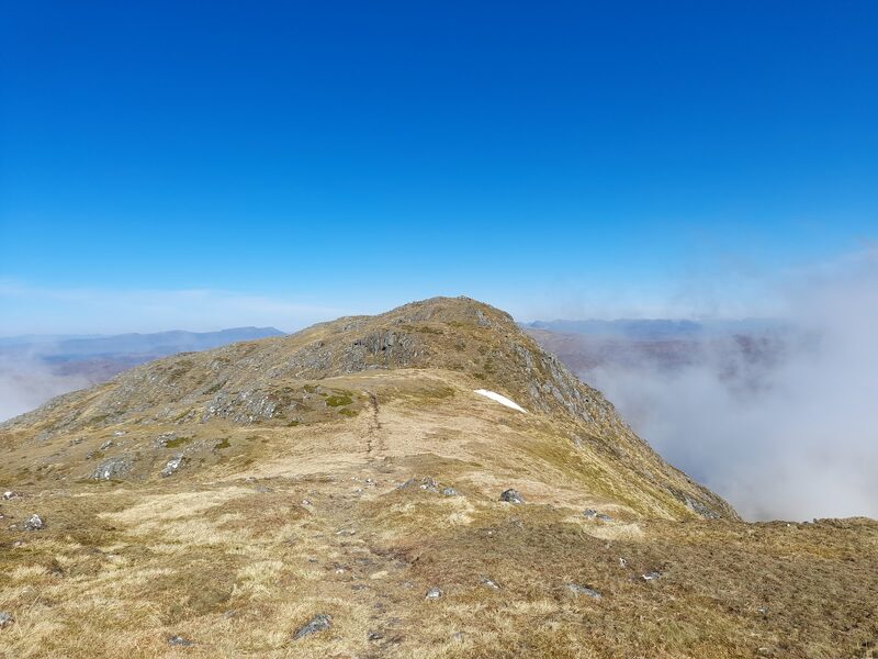 A grassy ridge on A' Ghlas-bheinn above a sea of cloud, under a deep blue sky.