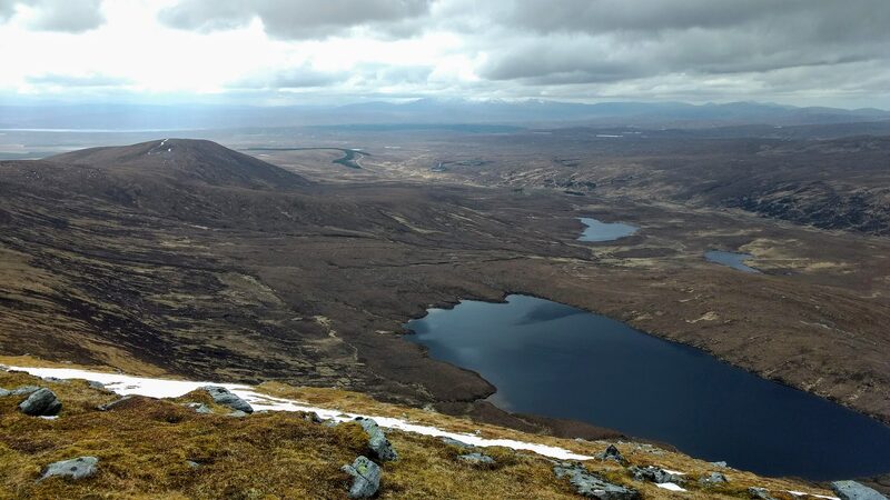 Dark lochans in the moor far below Ben Klibreck's ridge, a strip of old snow in the foreground.