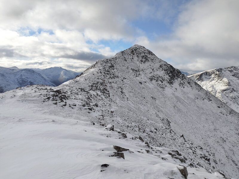 A pointed summit under snow seen along the ridge, another snowy hill behind it.