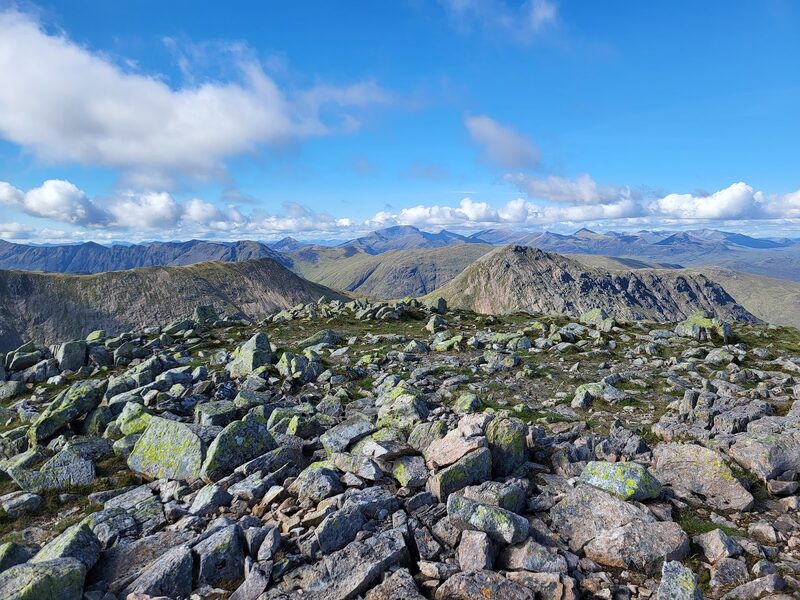 The top's field of green-lichened boulders, with a ridge of hills across the glen in sun.
