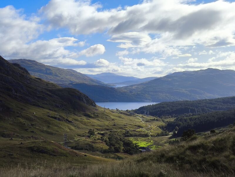 Looking back from the lower slopes of Ben Vane down a green glen to a loch, with hills and cloud beyond.
