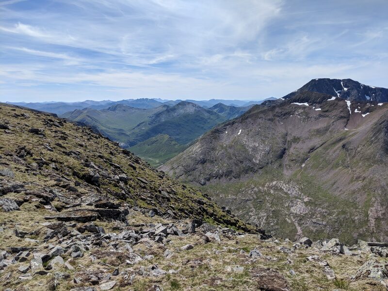 From a bouldery slope of Aonach Mòr, a red-brown ridge across a deep glen and a dark, snow-patched peak behind it.