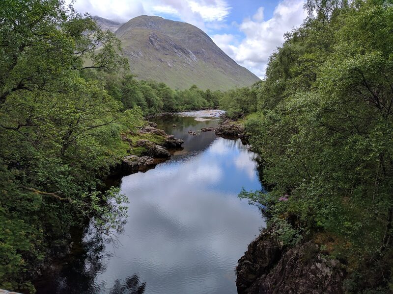 A still, rocky pool of the river between birches with the hill's broad cone above.